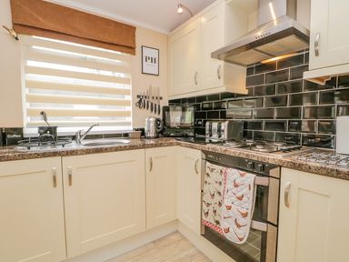 A kitchen with cream cabinets black tiled backsplash and stainless steel oven and appliances at Pheasant's Nest Kirkstone 11 Limefitt Park near Windermere