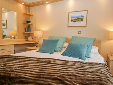 A bedroom with a bed pillows lamps a vanity mirror and framed painting at Pheasant's Nest Kirkstone 11 Limefitt Park near Windermere