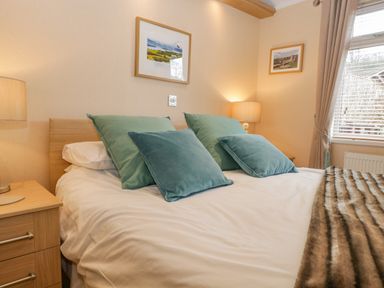A bedroom with a double bed blue and green cushions bedside tables lamps and framed pictures on walls at Pheasant's Nest Kirkstone 11 Limefitt Park near Windermere