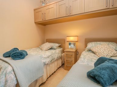 A bedroom with two single beds a nightstand with a lamp overhead cabinets and folded towels on each bed at Pheasant's Nest Kirkstone 11 Limefitt Park near Windermere