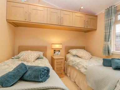 A bedroom with two single beds a nightstand and overhead cabinets at Pheasant's Nest Kirkstone 11 Limefitt Park near Windermere