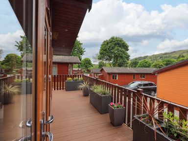 A wooden balcony with planters and a view of wooden cabins and trees at Pheasant's Nest Kirkstone 11 Limefitt Park near Windermere
