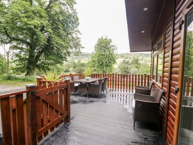 A wooden deck with outdoor table and chairs surrounded by trees at Ambleside Lodge Fellside 3 Limefitt Park near Windermere