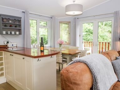 A kitchen and dining area with a wooden table, chairs, and a brown sofa with a blanket at Ambleside Lodge Fellside 3 Limefitt Park near Windermere