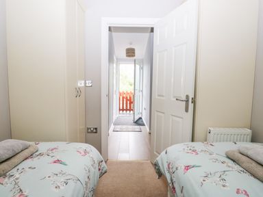 A bedroom with two single beds in front of wardrobes and a door leading to a hallway with a red gate at Ambleside Lodge Fellside 3 Limefitt Park near Windermere