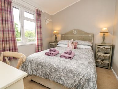 A bedroom with a double bed two bedside tables and lamps near a window with pink plaid curtains at Ambleside Lodge Fellside 3 Limefitt Park near Windermere