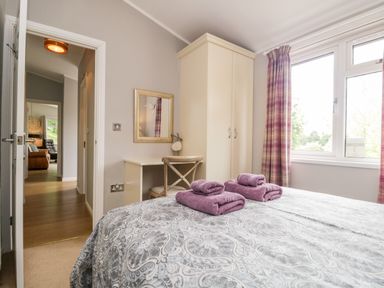 A bedroom with a bed with folded towels a wardrobe a chair and desk and a window with curtains at Ambleside Lodge Fellside 3 Limefitt Park near Windermere