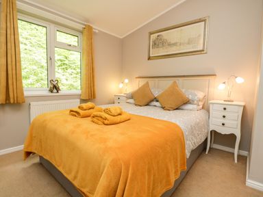 A bedroom with a double bed yellow bedding and towels two bedside tables with lamps and a window with yellow curtains at Ambleside Lodge Fellside 3 Limefitt Park near Windermere