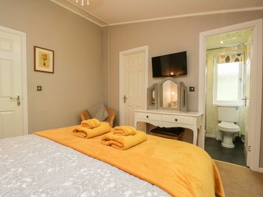 A bedroom with a bed covered with towels a dressing table a wall-mounted TV and an en suite bathroom at Ambleside Lodge Fellside 3 Limefitt Park near Windermere