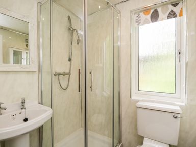 A bathroom with a glass shower enclosure a white sink a toilet and a window with a patterned blind at Ambleside Lodge in Fellside 3 Limefitt Park near Windermere