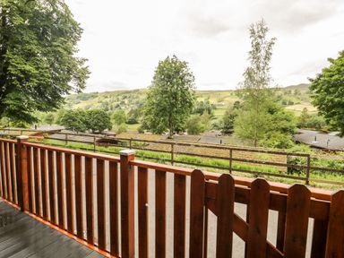 A wooden balcony railing overlooking trees rooftops and hills at Ambleside Lodge Fellside 3 Limefitt Park near Windermere