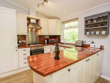 A kitchen with white cabinets a wooden countertop and a window at Ambleside Lodge Fellside 3 Limefitt Park near Windermere