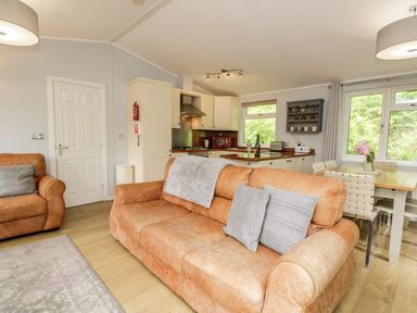 A living room with brown sofas and a kitchen with white cabinets and a dining table at Ambleside Lodge Fellside 3 Limefitt Park near Windermere