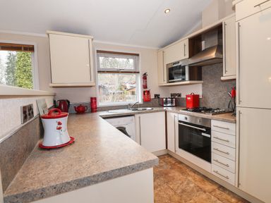 A kitchen with a countertop stove oven microwave washing machine and red kitchen accessories at Robins Nest Bowness 71 White Cross Bay near Windermere