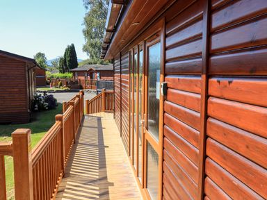 A wooden deck with railings attached to a wooden cabin with other cabins and trees in the background at Robins Nest in Bowness 71 White Cross Bay near Windermere