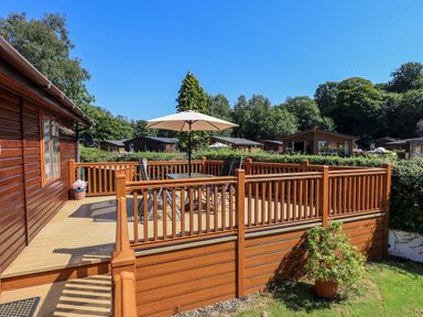 A wooden deck with a table umbrella and chairs attached to a cabin at Robins Nest in Bowness 71 White Cross Bay near Windermere
