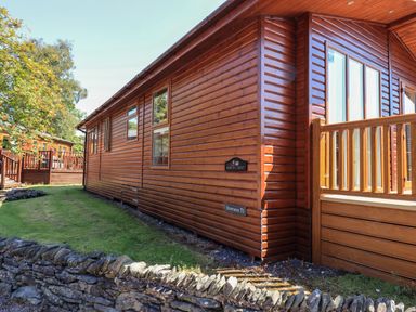Exterior view of a wooden cabin with windows a small grassy yard and a stone wall at Robins Nest in Bowness 71 White Cross Bay near Windermere
