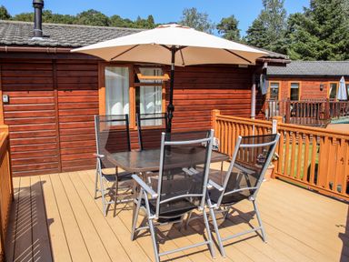 An outdoor deck with a table umbrella and chairs outside a wooden cabin at Robins Nest Bowness 71 White Cross Bay near Windermere