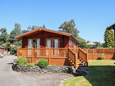 A wooden cabin with a deck and stairs surrounded by trees and grass at Robins Nest Bowness 71 White Cross Bay near Windermere