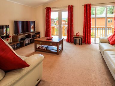 A living room with two white sofas with red cushions a wooden coffee table and entertainment unit with a tv at Robin's Nest in Bowness 71 White Cross Bay near Windermere