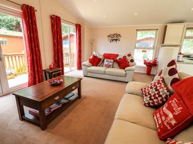 A living room with two beige sofas red cushions a wooden coffee table and red curtains at Robins Nest Bowness 71 White Cross Bay near Windermere