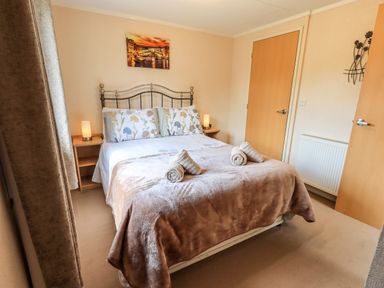 A bedroom with a double bed two bedside tables with lamps a painting on the wall and two rolled towels on the bed at Robins Nest Bowness 71 White Cross Bay near Windermere