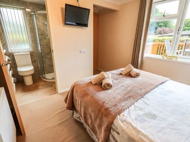 A bedroom with a bed, folded towels on the bed, a wall-mounted TV, an ensuite bathroom with a toilet and shower, and a window with a view outside at Robins Nest in Bowness 71 White Cross Bay near Windermere