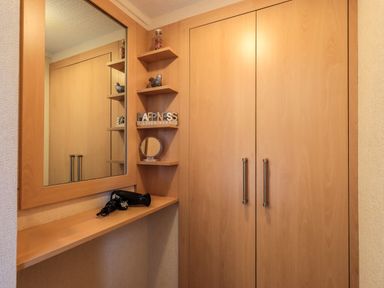 A corner with a large mirror above a shelf holding a hair dryer wooden cabinets and small wall shelves with decorations at Robins Nest in Bowness 71 White Cross Bay near Windermere