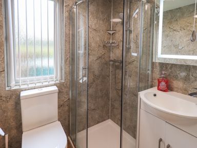 A bathroom with a toilet, glass shower enclosure, sink with cabinet, and a window with vertical blinds at Robins Nest Bowness 71 White Cross Bay near Windermere