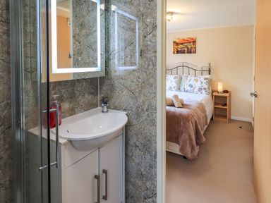 A bathroom with a sink and mirror next to a bedroom with a bed a bedside table and lamp at Robins Nest Bowness 71 White Cross Bay near Windermere