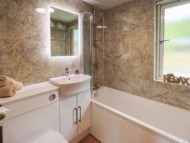 A bathroom with a bathtub a sink with cabinet towels on the counter and a window with a relax sign at Robins Nest Bowness 71 White Cross Bay near Windermere