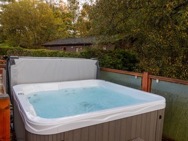 An outdoor hot tub with water inside on a wooden deck surrounded by trees at Thirlmere View Thirlmere 6 White Cross Bay near Windermere