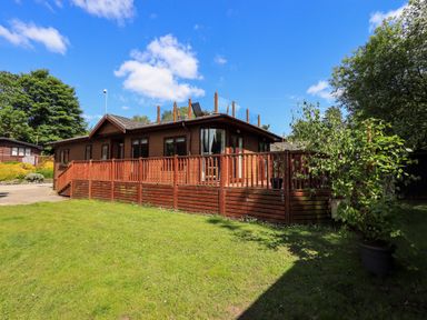 A wooden house with a raised deck and glass railings on the roof surrounded by grass and trees at Thirlmere View Thirlmere 6 White Cross Bay near Windermere