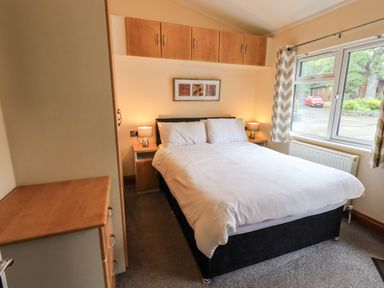 A bedroom with a double bed two bedside tables with lamps a chest of drawers wooden cabinets above the bed and a window with curtains at Thirlmere View Thirlmere 6 White Cross Bay near Windermere