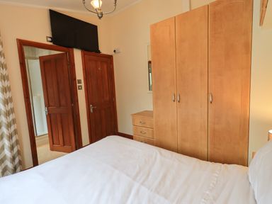 A bedroom with a bed a wooden wardrobe wooden doors and a wall mounted television at Thirlmere View in Thirlmere 6 White Cross Bay near Windermere