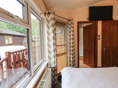 A bedroom with a bed a window with curtains a wooden door a wall-mounted television and a radiator at Thirlmere View Thirlmere 6 White Cross Bay near Windermere