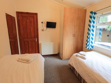 A bedroom with two single beds a wardrobe a wall-mounted television a radiator and a window with curtains at Thirlmere View Thirlmere 6 White Cross Bay near Windermere