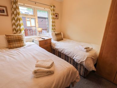 A bedroom with two single beds a nightstand with a lamp and window with patterned curtains at Thirlmere View in Thirlmere 6 White Cross Bay near Windermere