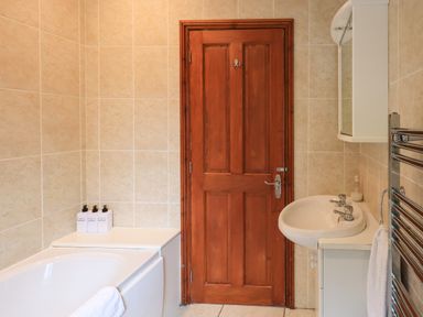 A bathroom with a wooden door a bathtub a sink with a cabinet and a towel rail at Thirlmere View Thirlmere 6 White Cross Bay near Windermere
