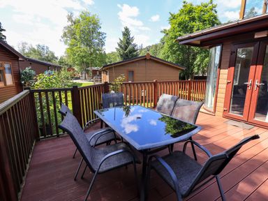An outdoor wooden patio with a glass table and six chairs at Thirlmere View Thirlmere 6 White Cross Bay near Windermere