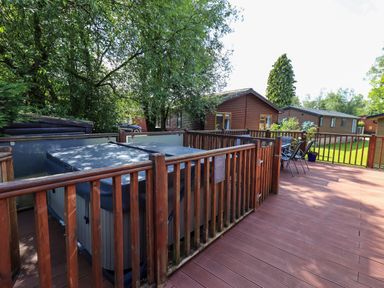 An outdoor deck with a hot tub enclosed by wooden railings and a seating area with chairs and a table at Thirlmere View Thirlmere 6 White Cross Bay near Windermere