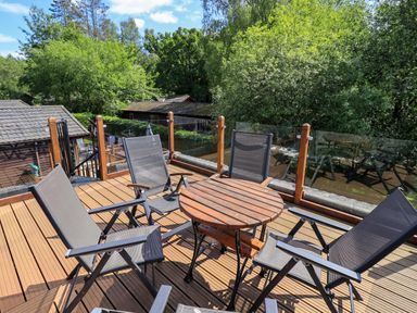 A wooden deck with a round table and four chairs surrounded by glass railings and trees at Thirlmere View Thirlmere 6 White Cross Bay near Windermere