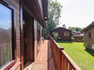 A wooden deck with railing attached to a wooden cabin overlooking a grassy yard with other wooden cabins at Thirlmere View in Thirlmere 6 White Cross Bay near Windermere