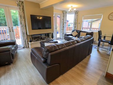 A living room with brown leather sofas a mounted TV and two sets of glass doors at Thirlmere View Thirlmere 6 White Cross Bay near Windermere