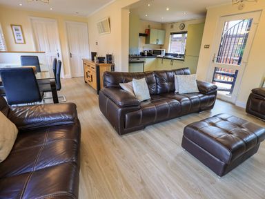 A living room with brown leather sofas and cushions next to a kitchen and dining area at Thirlmere View in Thirlmere 6 White Cross Bay near Windermere