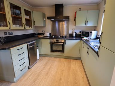 A kitchen with light green cabinets black countertops a gas stove oven dishwasher microwave kettle and toaster at Thirlmere View Thirlmere 6 White Cross Bay near Windermere