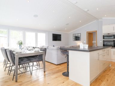 An open plan kitchen and dining area with a dining table set for six and a kitchen island with bar stools at Lakes Lodge Keswick Court 3 White Cross Bay near Windermere