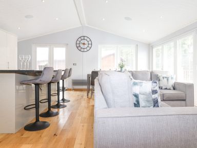 A living area with gray sofas and bar stools around a kitchen island at Lakes Lodge Keswick Court 3 White Cross Bay near Windermere