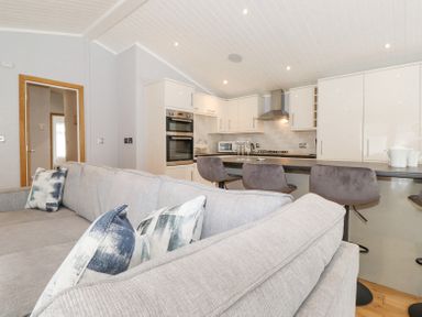An open plan living room and kitchen with a grey sofa and bar stools at Lakes Lodge Keswick Court 3 White Cross Bay near Windermere