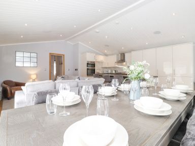 A dining table set with plates glasses and a flower vase in an open living room and kitchen at Lakes Lodge Keswick Court 3 White Cross Bay near Windermere